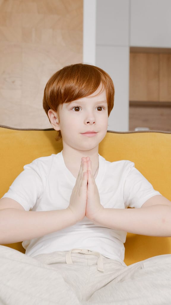 boy sitting in yellow chair with hands folded in yoga prayer position