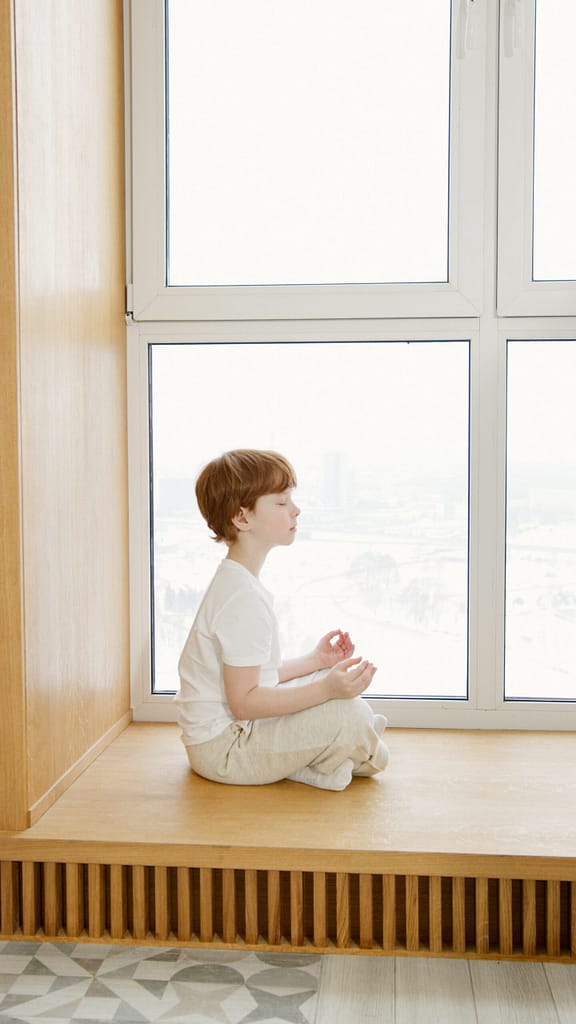 boy sitting by windowsill with eyes closed and legs cris-crossed