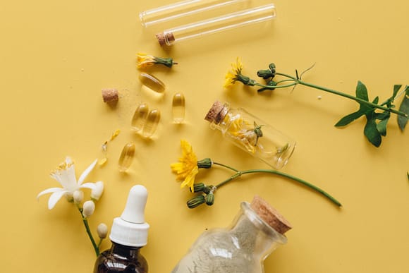transculent yellow pills, yellow and white flowers, and medicinal bottles against yellow background
