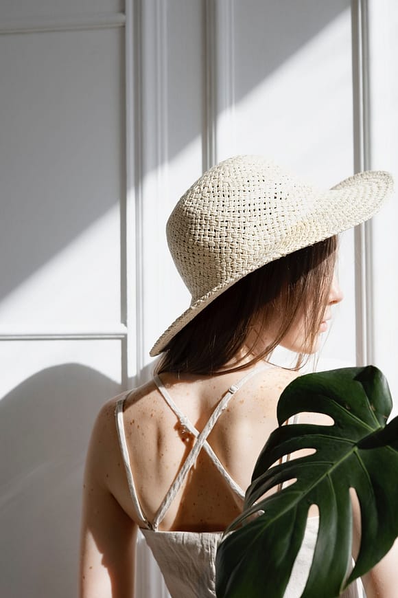 woman in sun hat with green leaf behind her