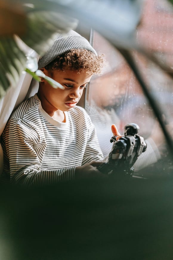 Black boy looking sad while holding a toy taken as a spy shot behind a plant