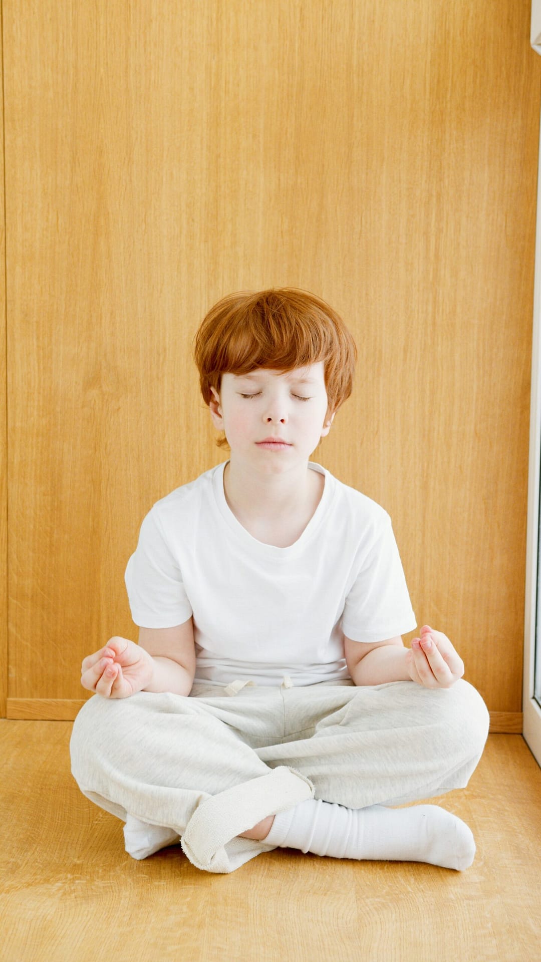 red headed boy in white clothes sitting down with eyes closed